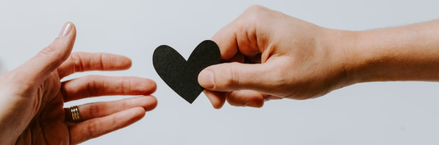 Persoon geeft een zwart papieren hart aan een andere persoon