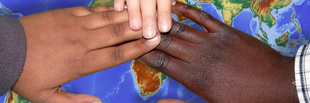 Drie kinderen leggen elk hand op wereldkaart 