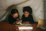twee kindjes lezen onder een zeil met een lampje